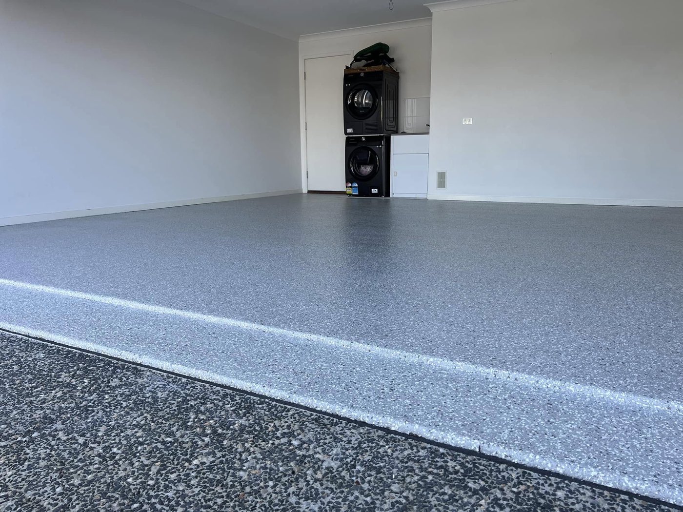 The same garage after coating, a deep grey and white flake floor with a crisp white edge line along the step down to the driveway.