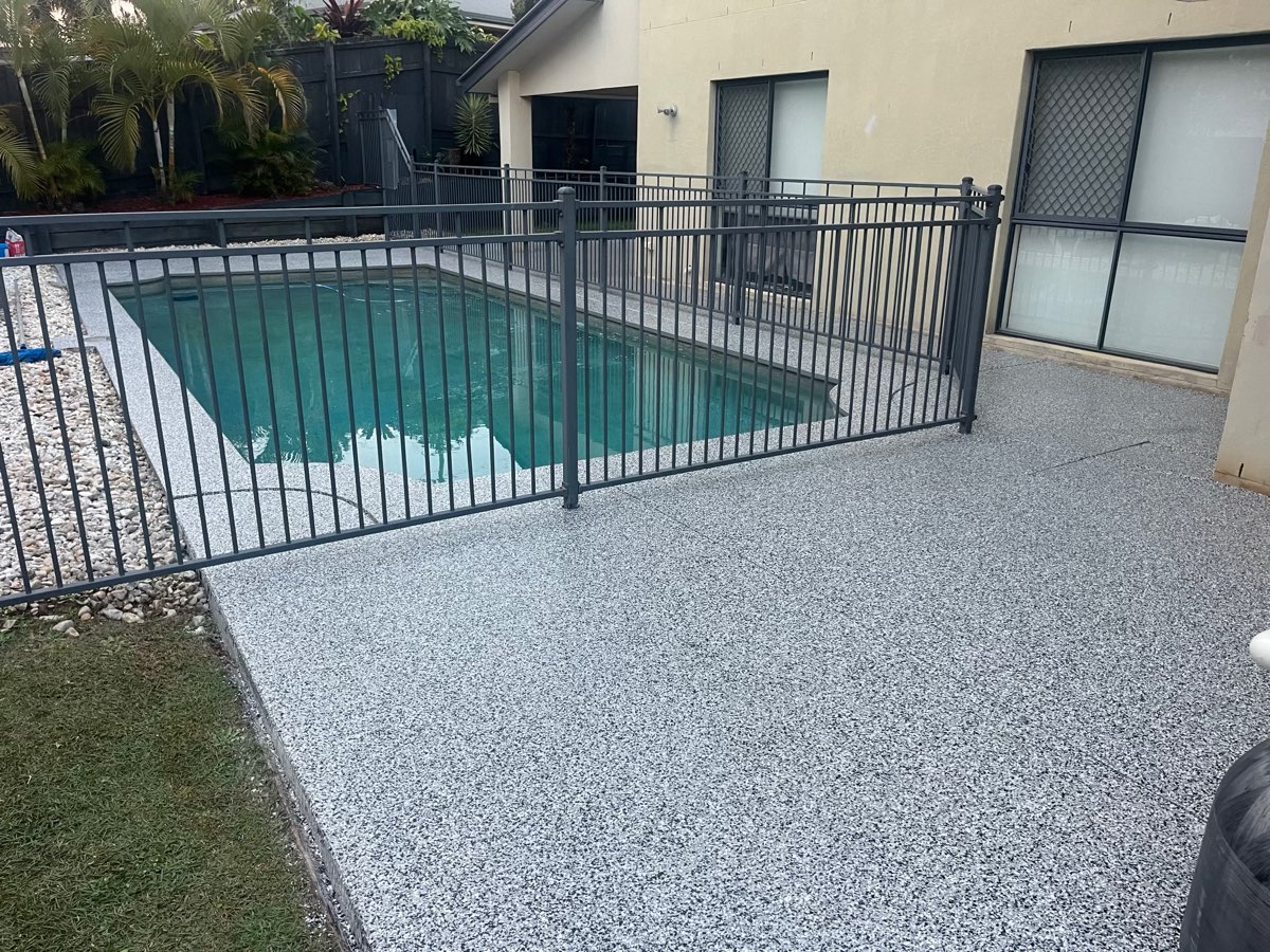Pool surround and side path coated in a grey and white flake finish, wrapping a small fenced plunge pool beside the lawn.
