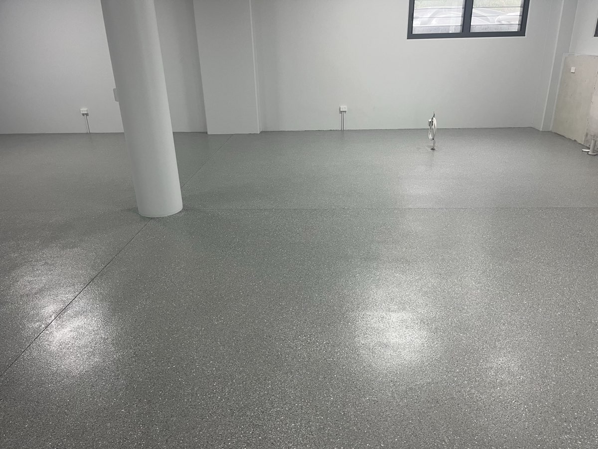 Downstairs room with a glossy grey flake floor running around a round white support column, white walls and a window above.