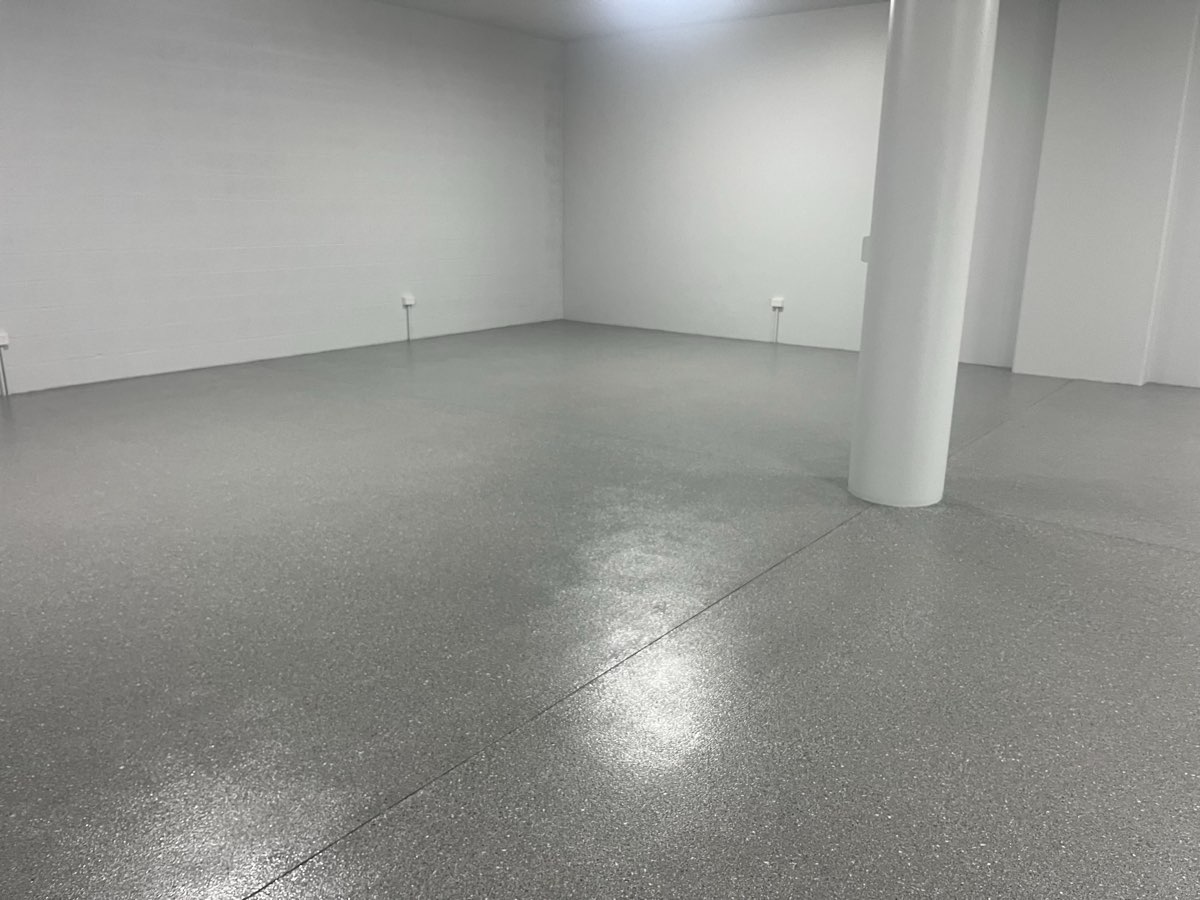 Wider view of a glossy grey flake floor in an empty downstairs space, the light catching it beside a round white column.